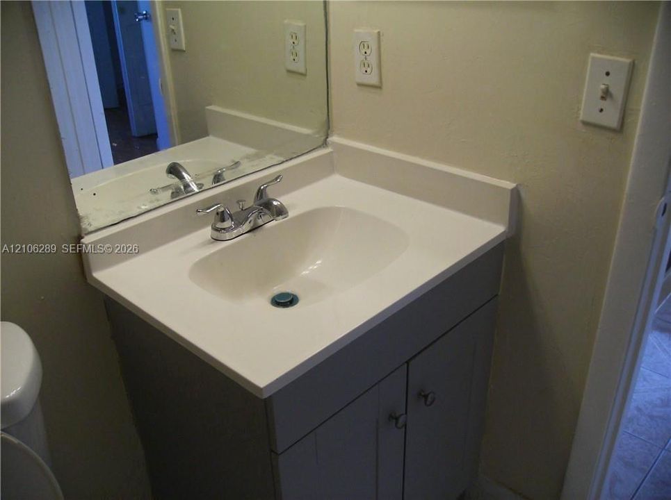 Vanity featuring a solid surface countertop with an integrated basin, chrome-finish dual-handle faucet, gray cabinetry, and a wall-mounted mirror