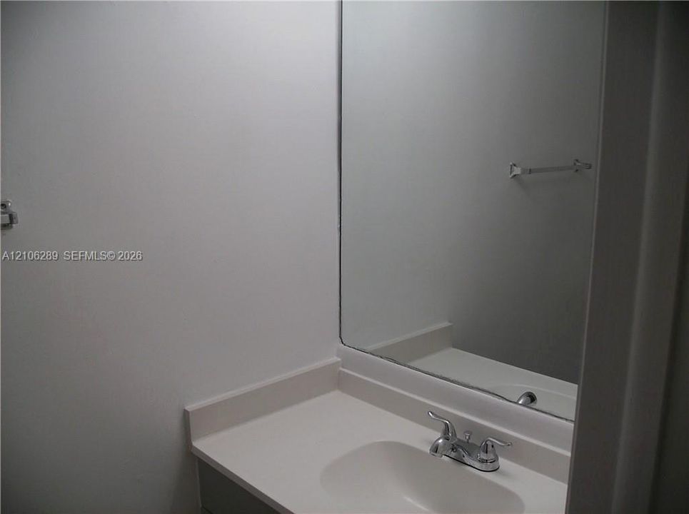 Vanity with integrated sink, solid surface countertop, chrome dual-handle faucet, and rectangular wall-mounted mirror with attached towel bar