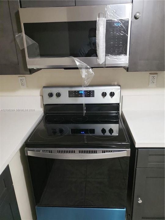 Kitchen featuring dark-toned cabinetry, stainless steel over-the-range microwave, electric range with a smooth black cooktop, and solid-surface countertops