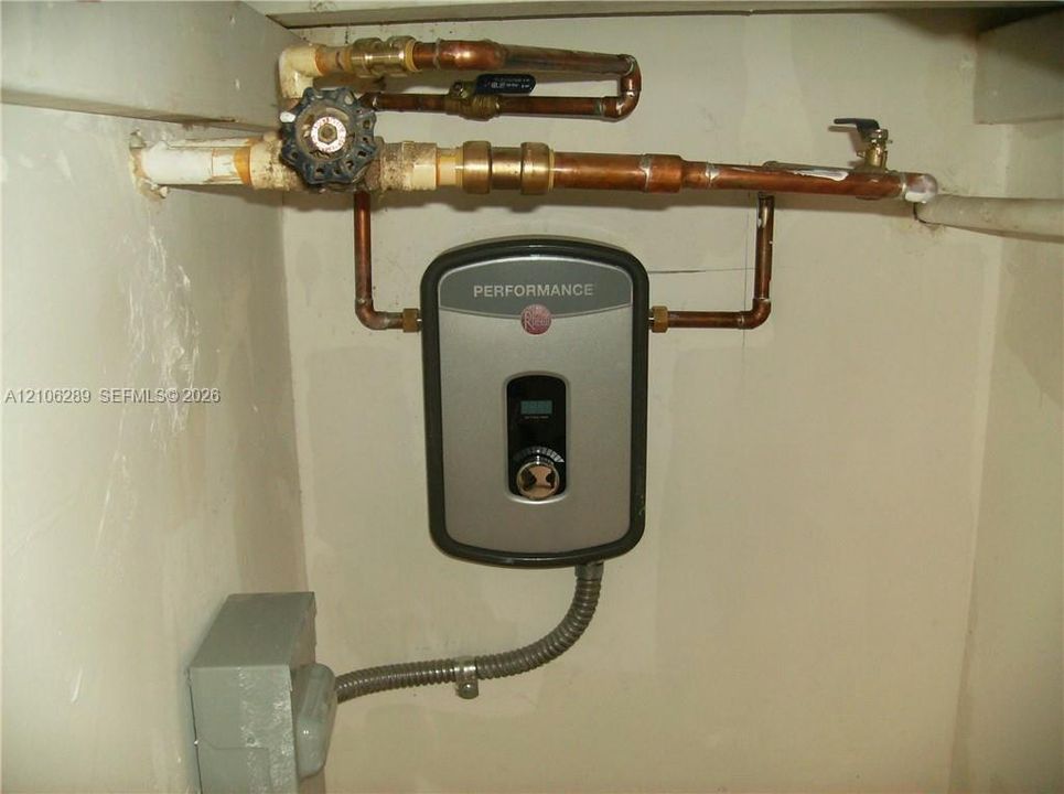 Tankless electric water heater featuring digital temperature controls, copper plumbing lines, and a shut-off valve