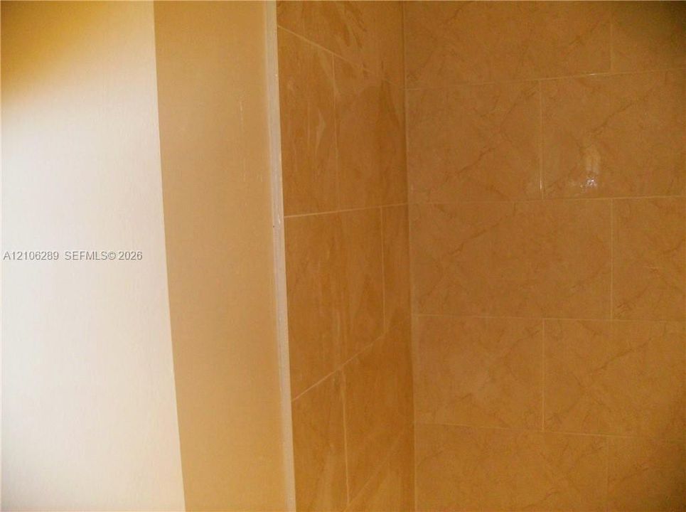 Neutral-toned wall finish with floor-to-ceiling tile surround featuring a subtle textured pattern