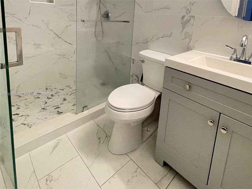 Bathroom featuring a walk-in glass-enclosed shower with tiled surround, stone-patterned floor tile, grey shaker-style vanity cabinet, and rectangular sink