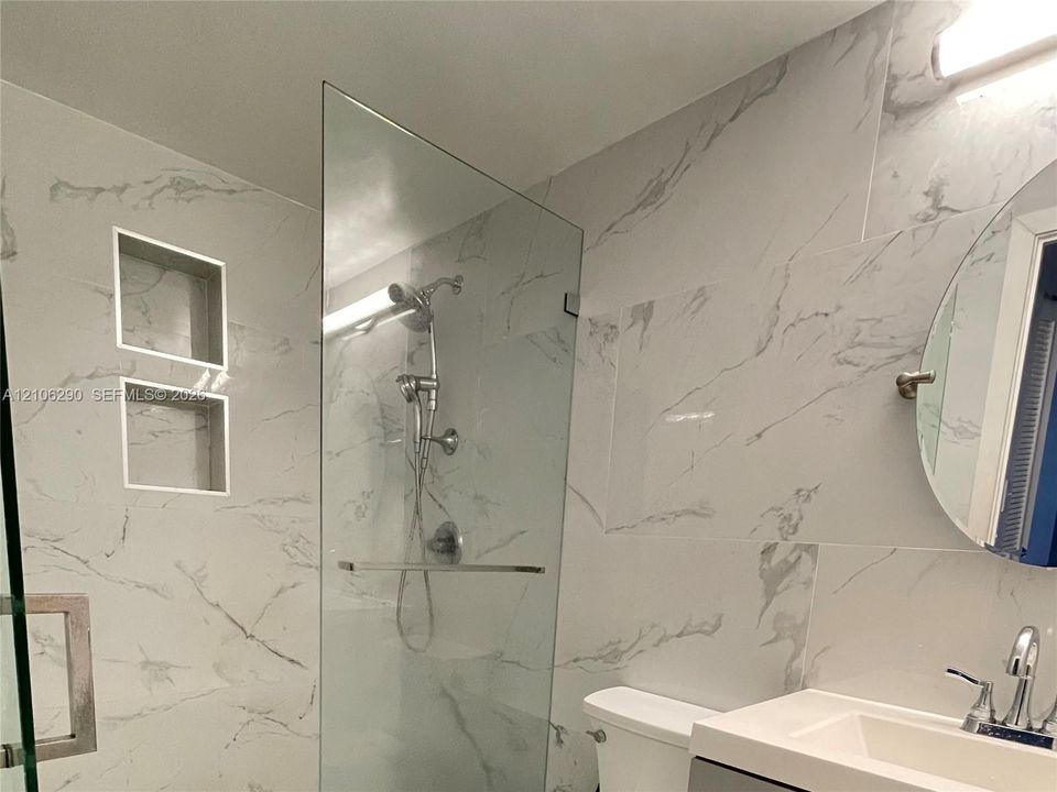 Walk-in shower featuring a frameless glass enclosure, dual built-in wall niches, large-format veined tile surround, and polished chrome fixtures