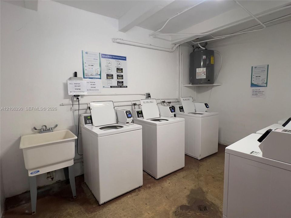 Utility space featuring multiple top-load washers, a basin sink with wall-mounted faucet, and a wall-mounted water heater