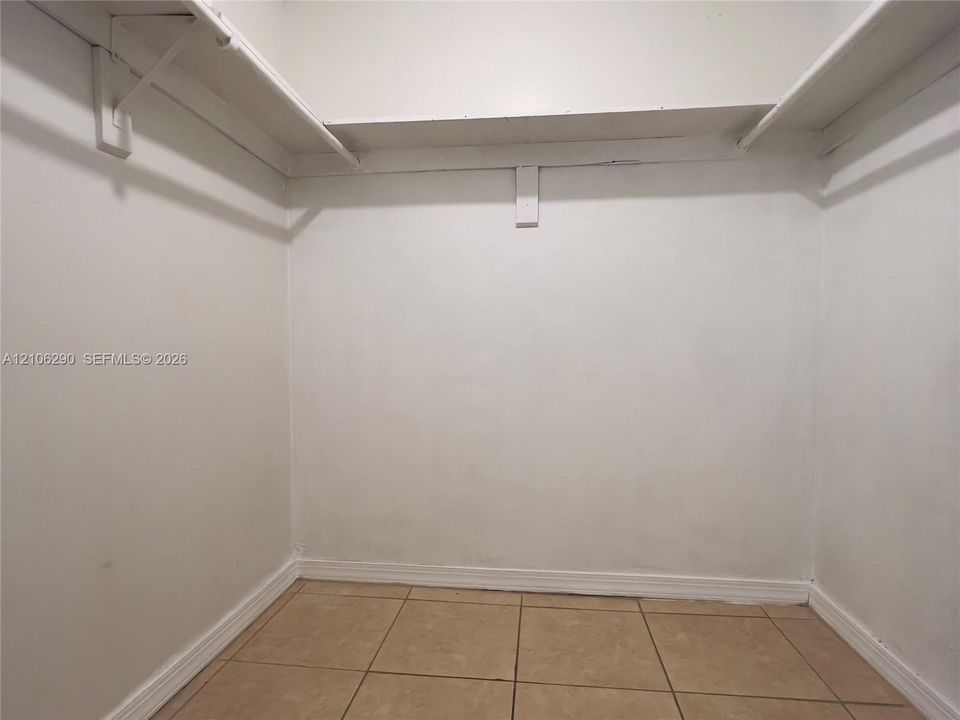 Walk-in storage space featuring ceramic tile flooring, neutral painted walls, and integrated wrap-around shelving with hanging rods