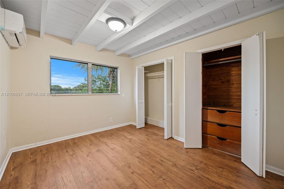 Room featuring a vaulted ceiling with exposed painted beams, wood-finish flooring, a horizontal sliding window, and built-in closet cabinetry with integrated shelving and drawers
