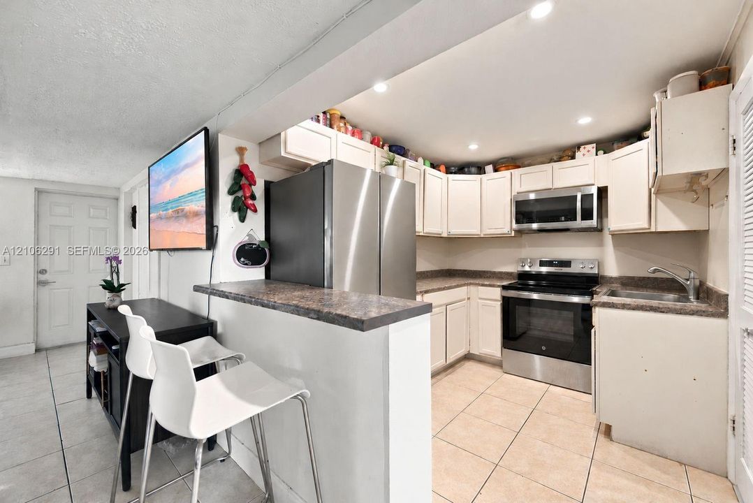 Kitchen featuring stainless steel appliances, white cabinetry, a breakfast bar with stone-finish countertop, and tile flooring
