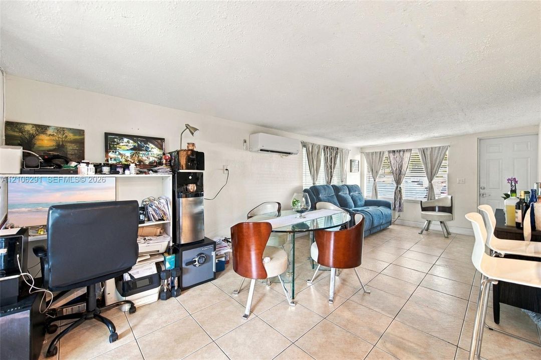Open-concept interior featuring neutral tile flooring, wall-mounted ductless climate control system, and large windows with horizontal blinds