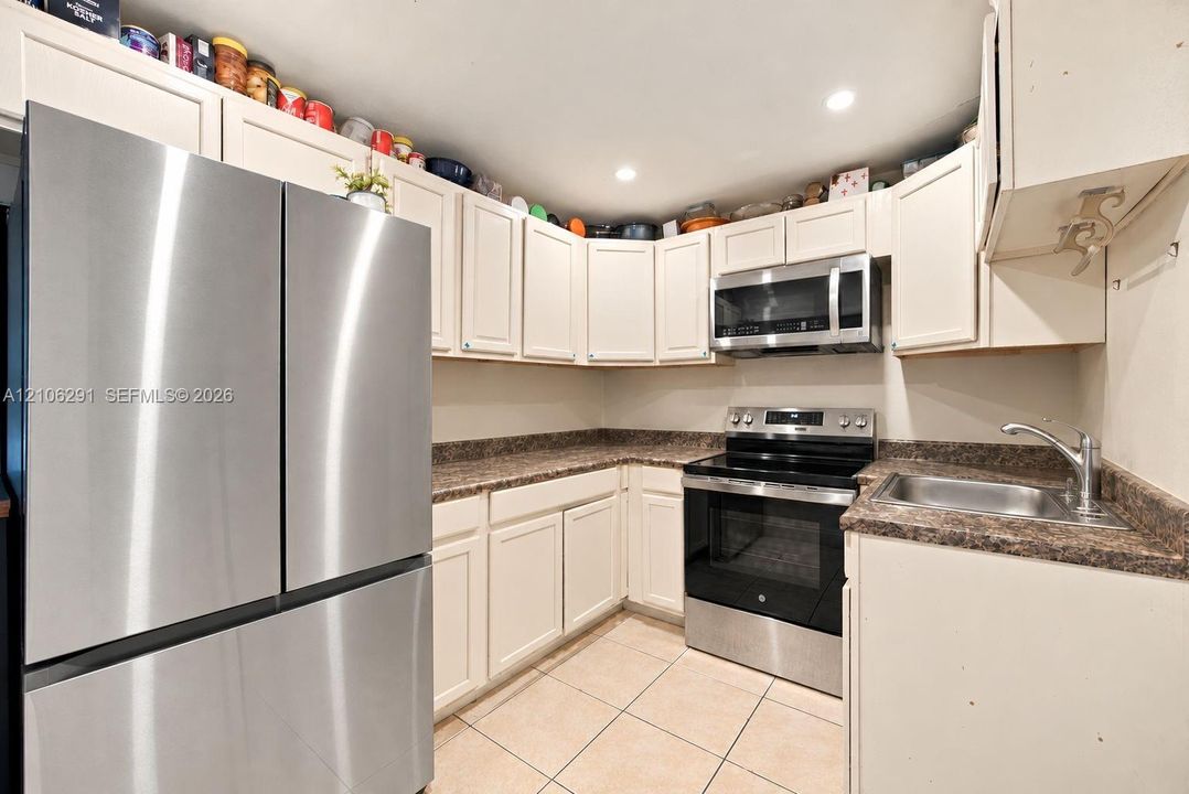 Kitchen featuring white cabinetry, stainless steel appliances, dark-toned laminate countertops, and tile flooring