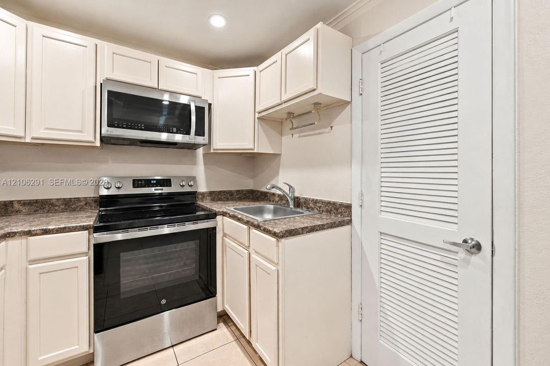 Kitchen featuring white cabinetry, stainless steel appliances, speckled laminate countertops, a single-basin sink, and tile flooring
