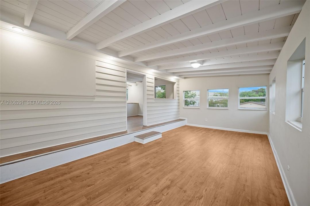 Interior space featuring exposed beam ceilings, wood-finish flooring, horizontal wall paneling, a raised platform level, and multiple windows