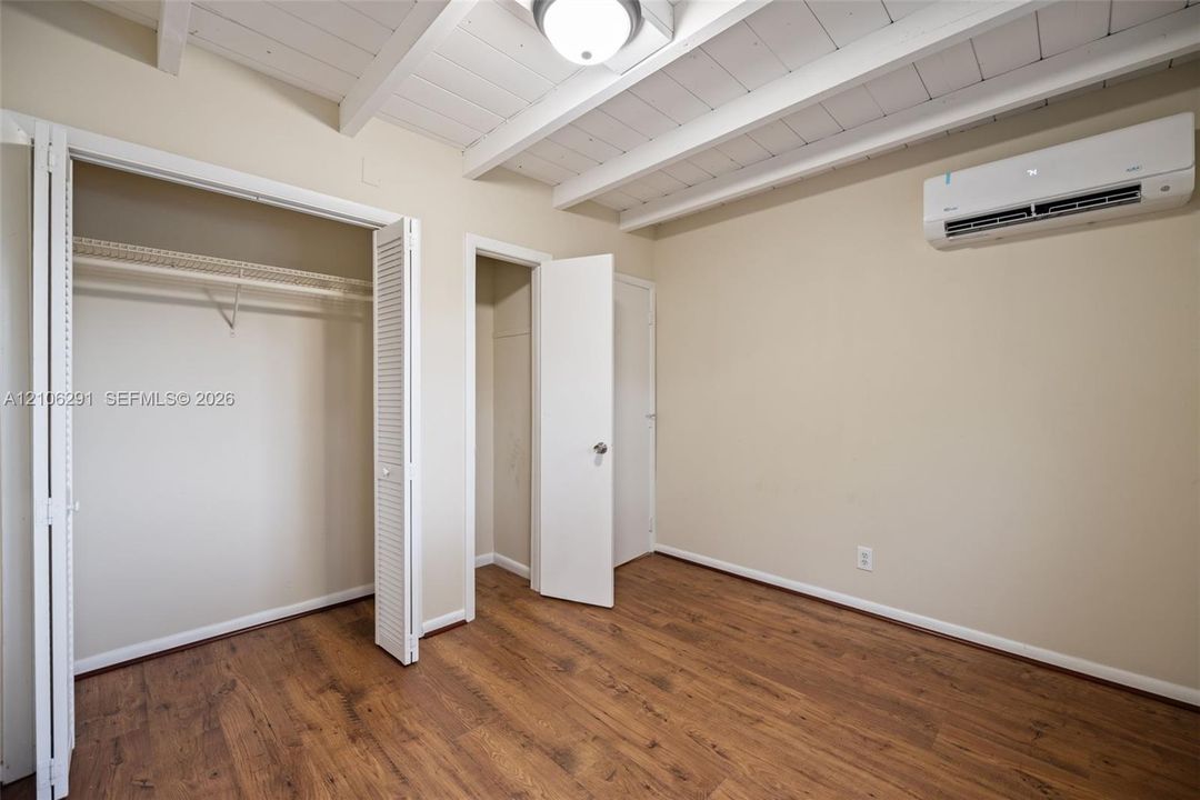 Room featuring wood-finish flooring, exposed painted ceiling beams, a wall-mounted ductless air conditioning unit, and dual closet storage options