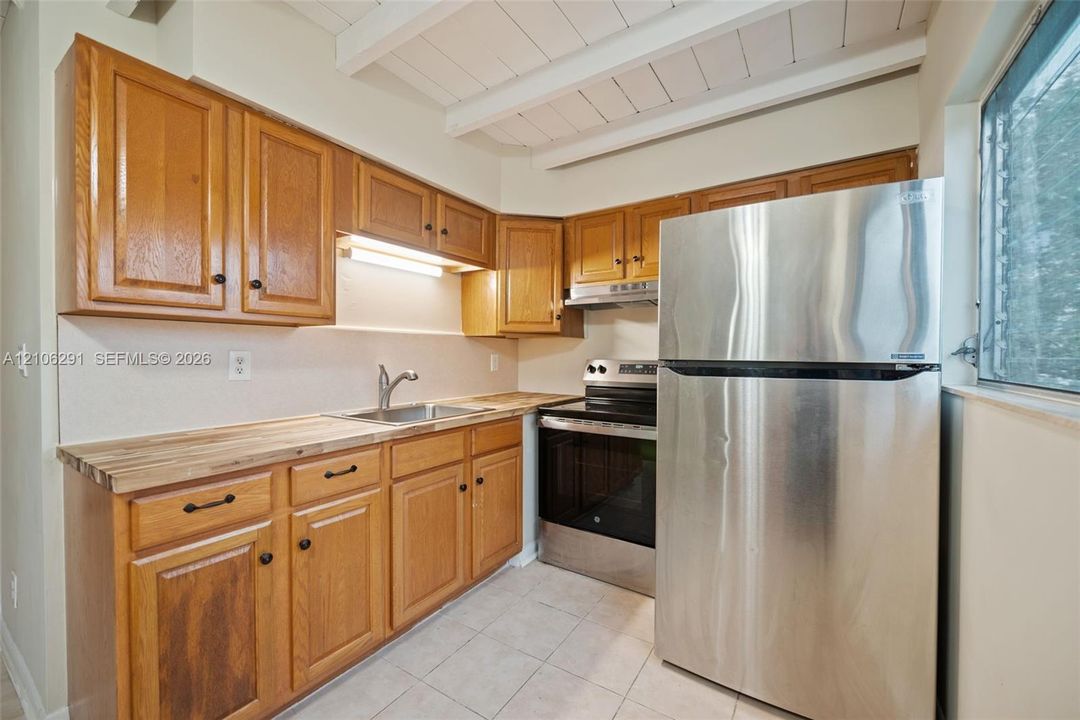 Kitchen featuring wood cabinetry, butcher block countertops, stainless steel appliances, tile flooring, and exposed ceiling beams