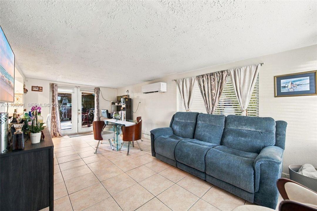 Open-concept room featuring light-toned tile flooring, wall-mounted ductless air conditioning unit, and glass-paneled double doors providing exterior access