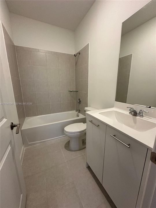Full bathroom featuring a white vanity cabinet with a stone-composite countertop, integrated sink, tile flooring, and a bathtub with tile surround