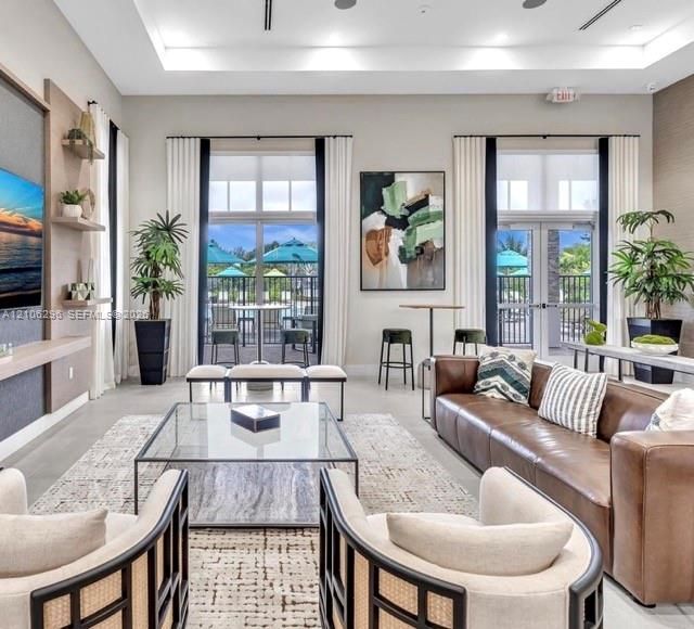 Common area featuring a double-tray ceiling with recessed lighting, built-in wall shelving, expansive windows, and dual sets of glass-paneled doors opening to an exterior patio