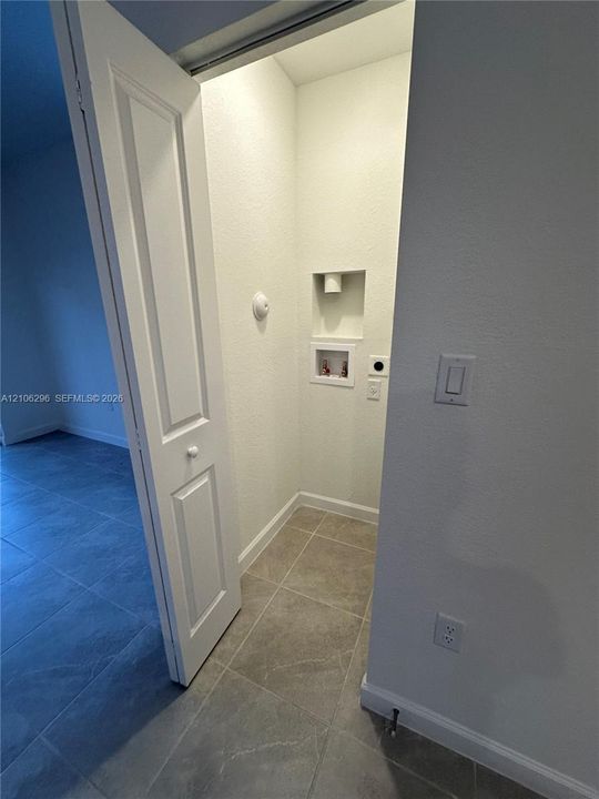 Utility closet featuring tile flooring, a recessed plumbing connection box, and a solid-panel door