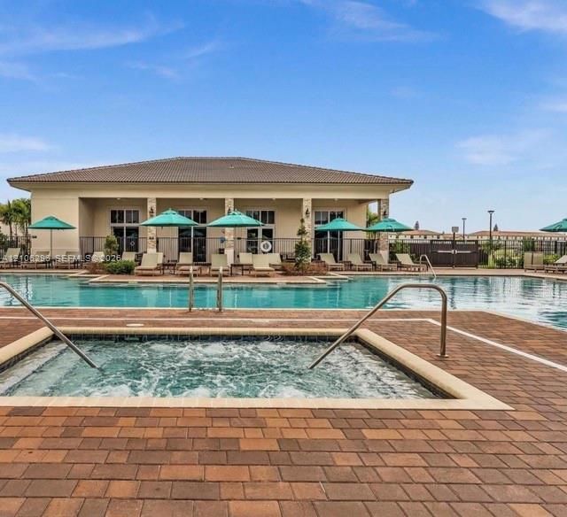 Outdoor pool area featuring a built-in spa, paver decking, covered clubhouse structure, and stone-accented support columns