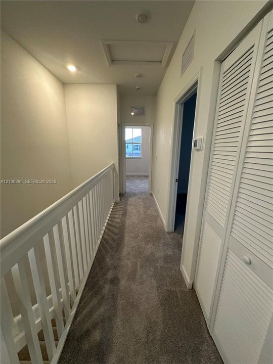 Hallway featuring neutral wall-to-wall carpeting, white railing with vertical balusters, and louvered closet doors