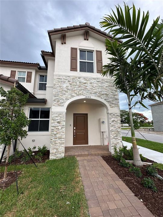 Stucco exterior featuring stacked stone accents, decorative window shutters, an arched covered entryway, and a paved walkway
