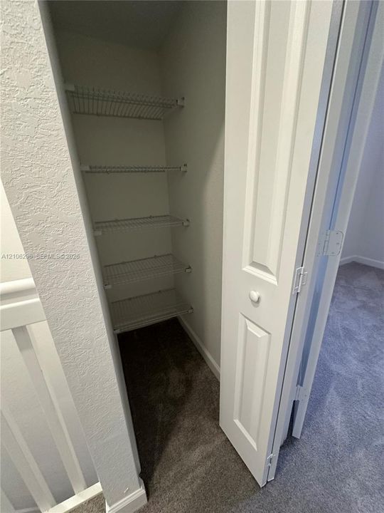 Storage closet featuring four white wire shelves and a hinged, paneled interior door