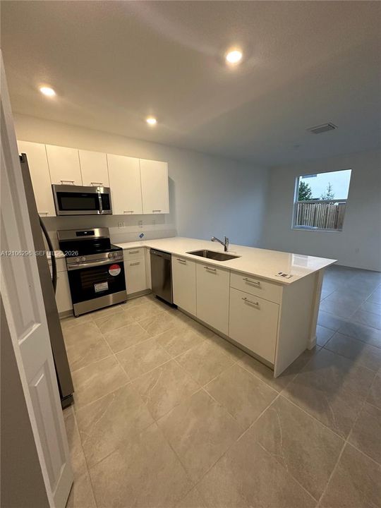 Kitchen featuring white flat-panel cabinetry, light-toned stone-finish countertops, stainless steel appliances, and large-format tile flooring