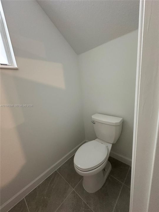 Enclosed space featuring porcelain toilet, tile flooring, and angled ceiling