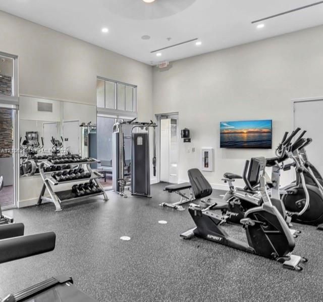 Fitness area featuring high ceilings, recessed lighting, expansive wall-to-wall mirrors, and durable rubberized flooring