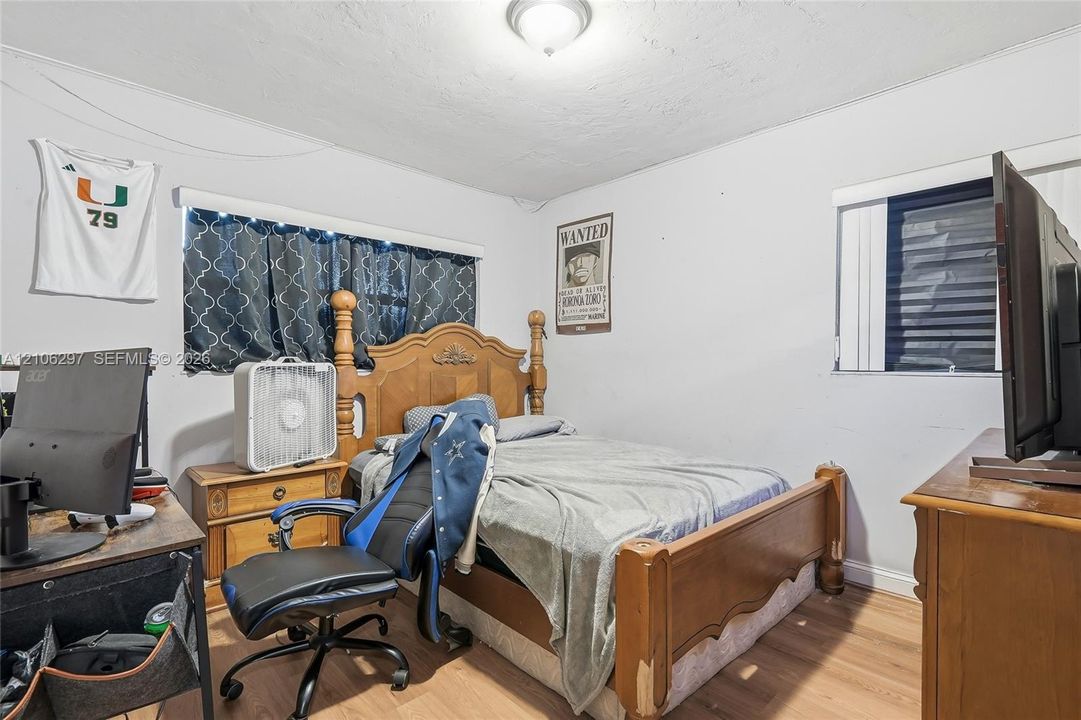 Bedroom featuring wood-finish flooring and two windows with horizontal blinds