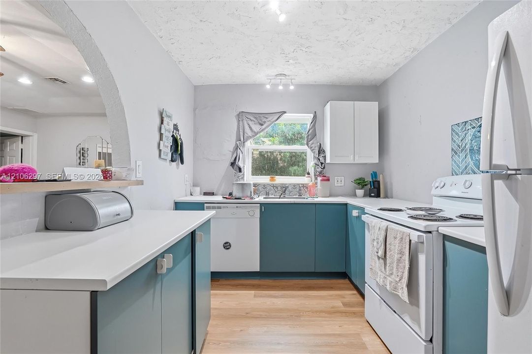 Kitchen featuring wood-finish flooring, white countertops, two-tone cabinetry, and a prominent arched architectural opening