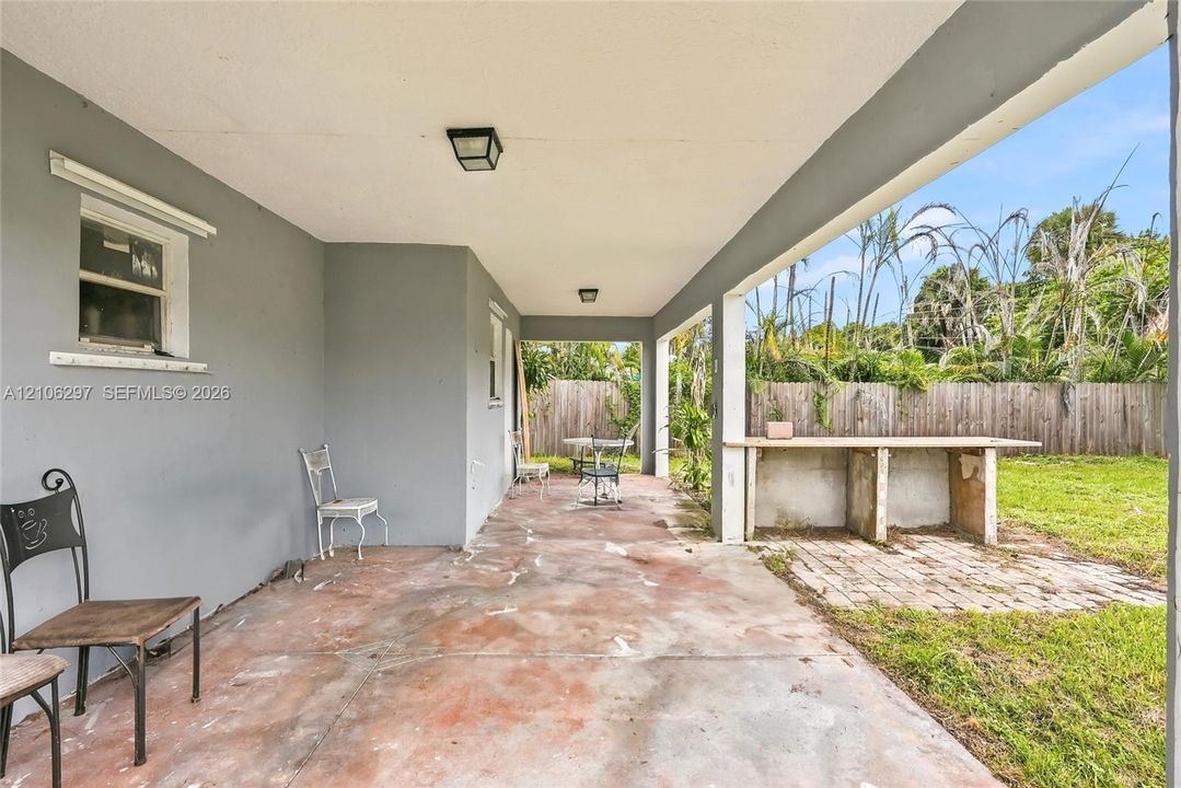 Covered patio featuring a concrete floor, built-in outdoor counter, and flush-mount lighting, overlooking a fenced backyard