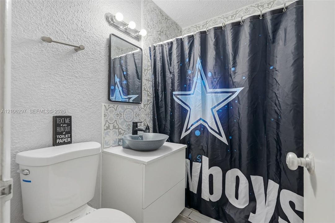 Bathroom featuring a white vanity cabinet, a grey circular vessel sink, matte black faucet, rectangular framed mirror, and decorative patterned tile backsplash