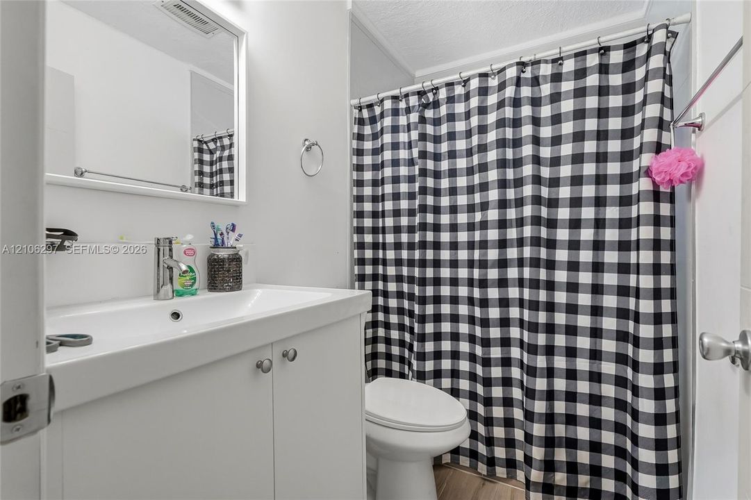 White vanity featuring a rectangular basin with a single-handle chrome faucet, a wall-mounted mirror, and a combination tub-shower with a chrome-finish shower rod