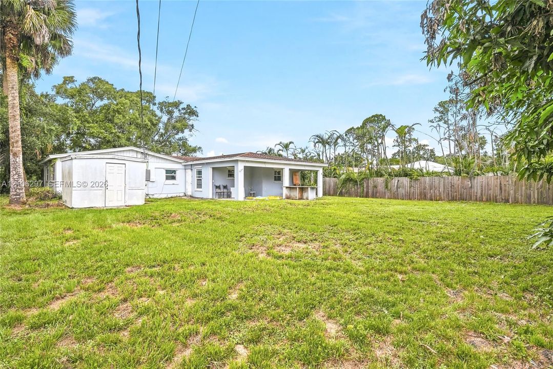 Expansive backyard featuring a covered patio, built-in outdoor masonry counter, detached storage structure, and perimeter wood fencing