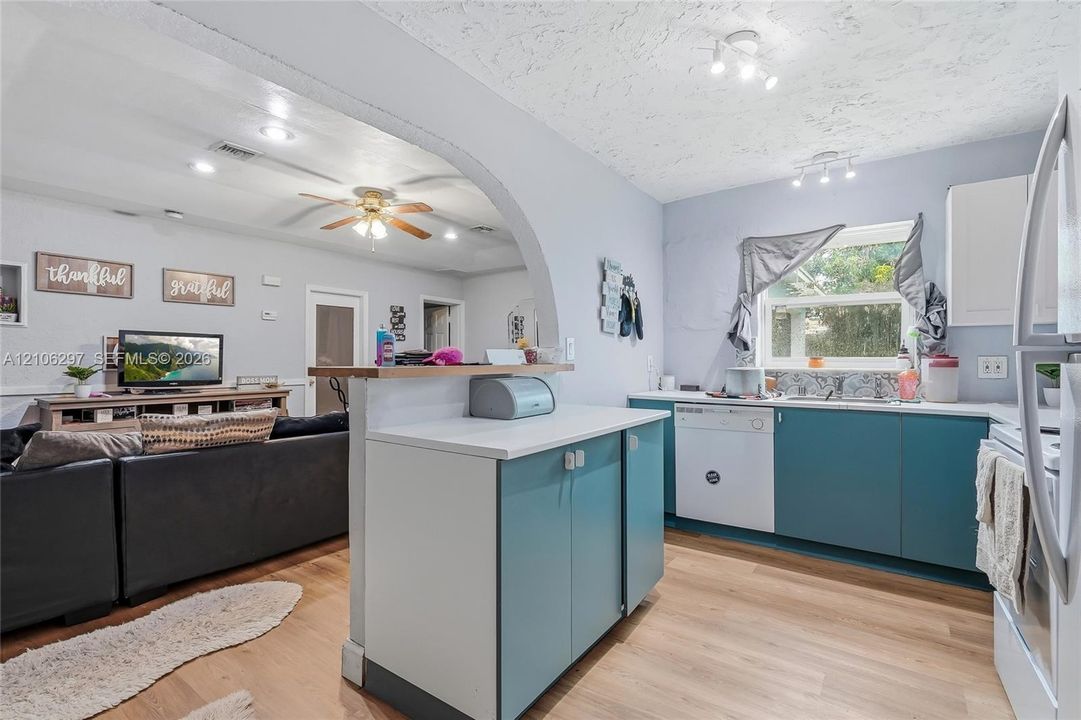 Kitchen featuring teal cabinetry, white countertops, wood-finish flooring, a decorative arched entryway, and integrated ceiling track lighting
