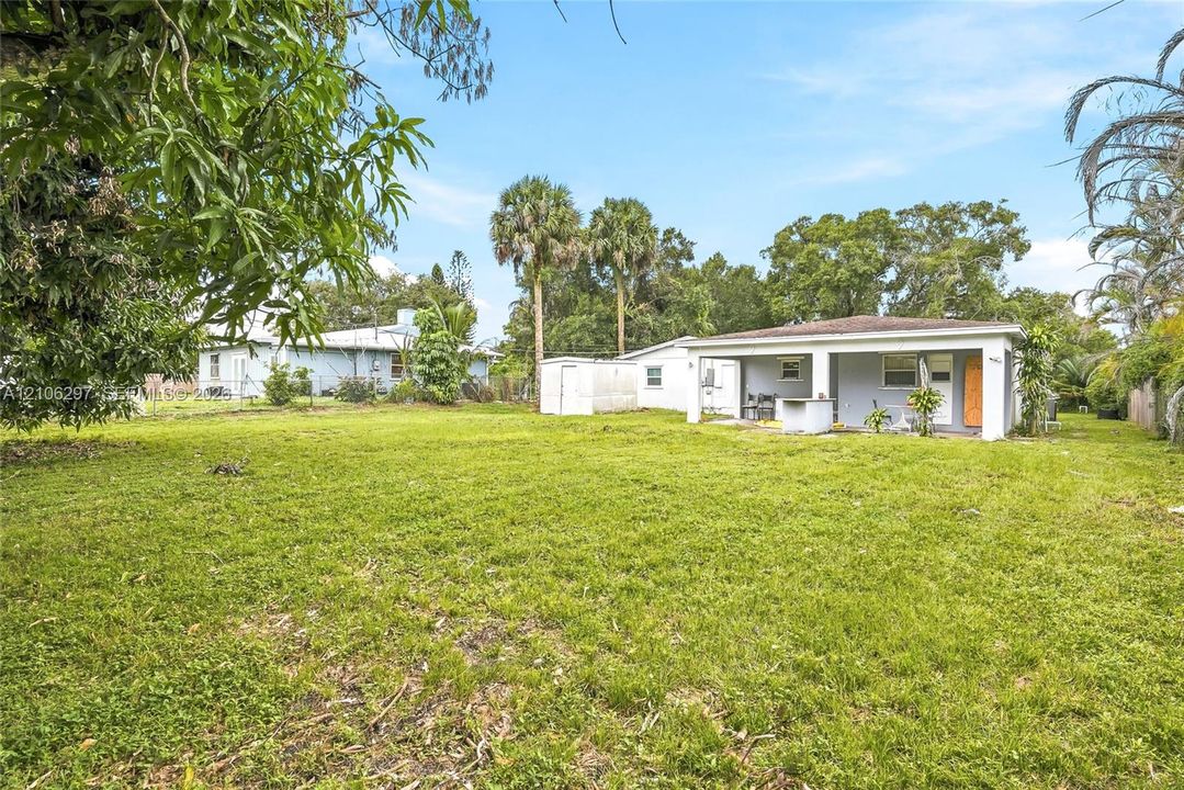 Expansive backyard featuring a sprawling lawn, mature trees, a detached storage structure, and a covered patio area