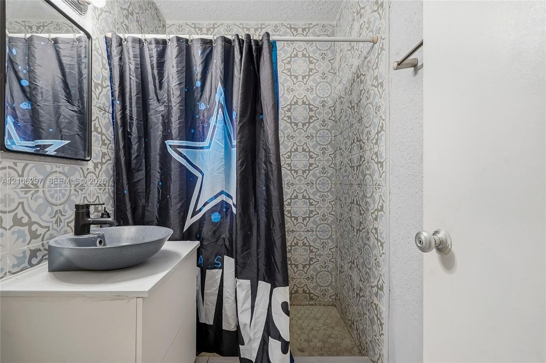 Bathroom featuring patterned wall tile, a white vanity cabinet, and a grey vessel sink with a black faucet