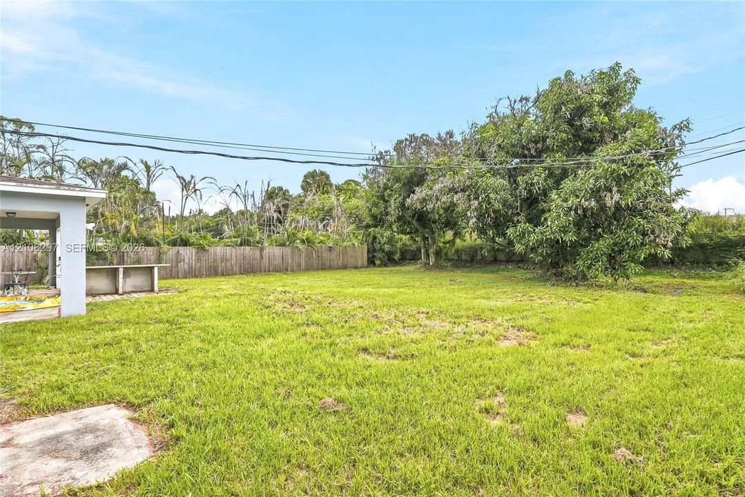 Spacious backyard featuring a concrete patio, built-in outdoor counter, wood fencing, and mature trees