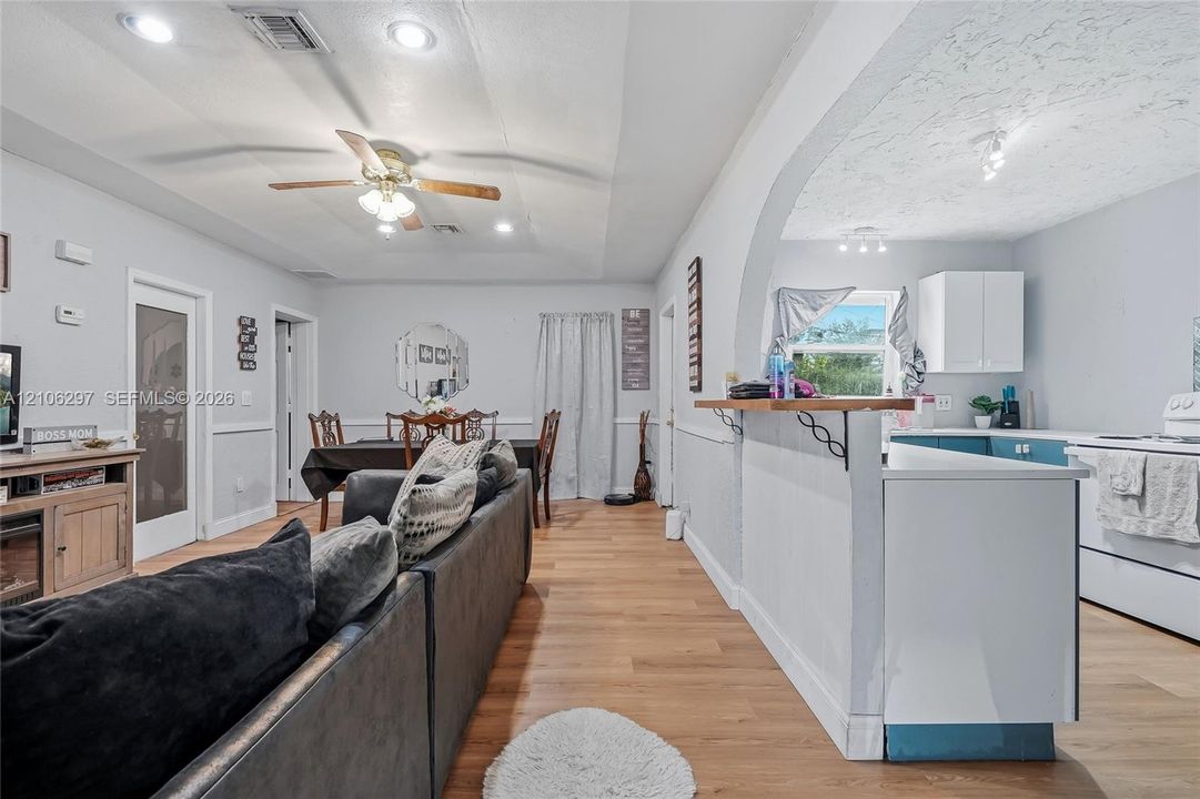 Open-concept interior featuring wood-finish flooring, a kitchen breakfast bar with decorative corbels, recessed lighting, a ceiling fan, and a wide arched entryway