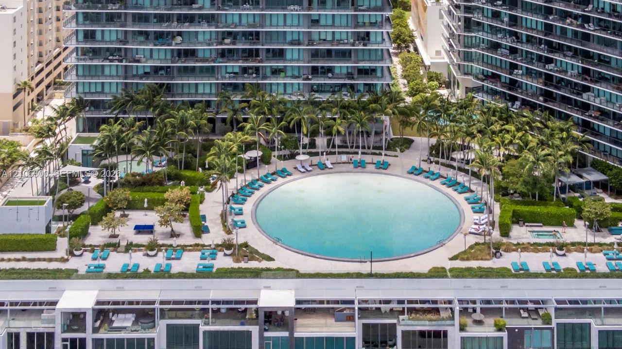 Circular swimming pool surrounded by paved decking, manicured landscaping, mature palm trees, and an integrated hot tub