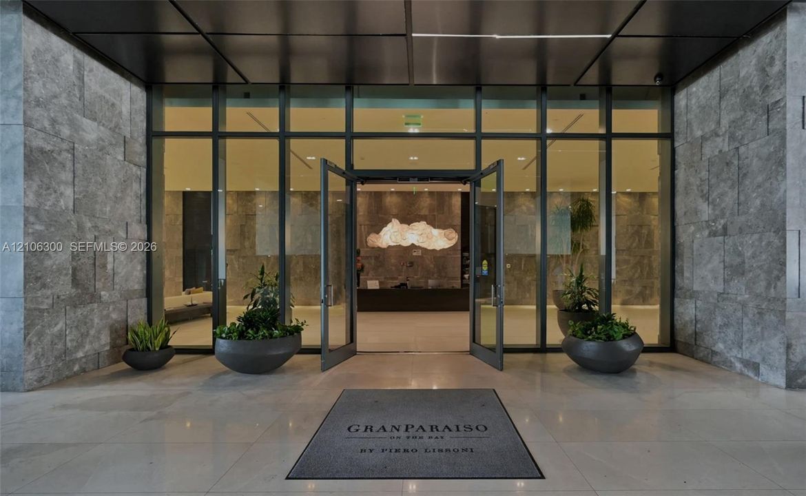 Expansive glass-paneled entrance framed by oversized textured stone cladding, polished stone flooring, and a sleek metal ceiling canopy