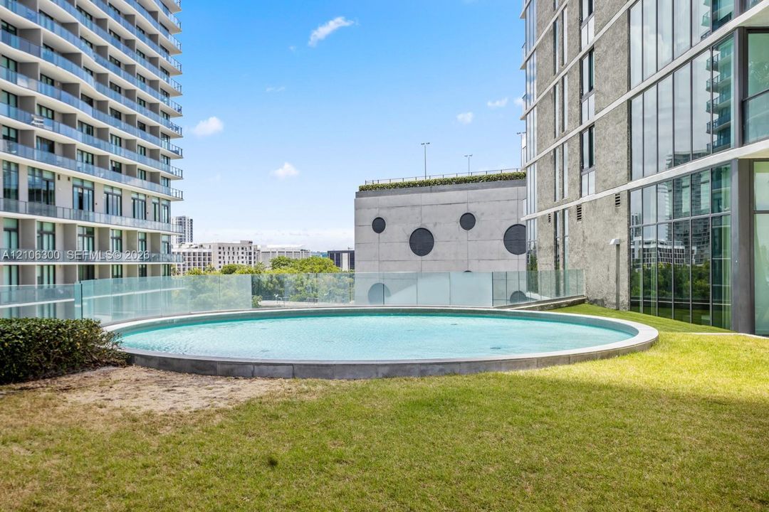 Circular outdoor pool featuring a glass balustrade surround and lawn landscaping