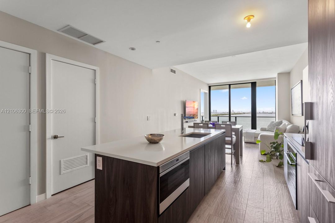Kitchen featuring a central island with a solid surface countertop, wood-finish cabinetry, built-in microwave, wood-finish flooring, and floor-to-ceiling windows