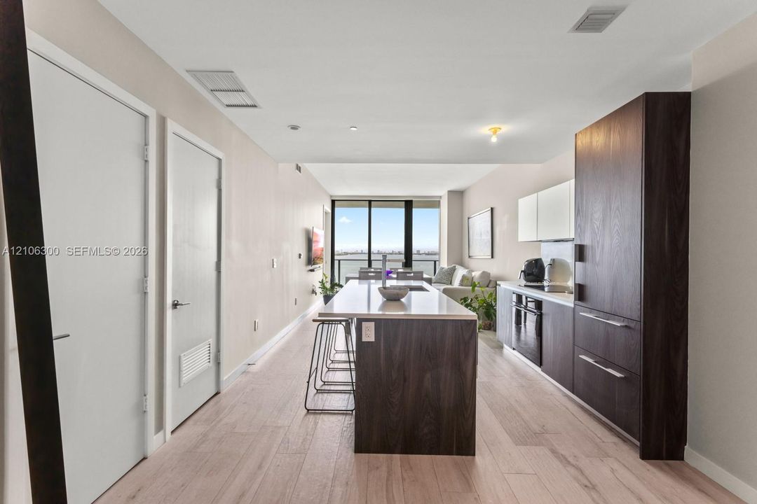 Kitchen featuring a central island with a solid-surface countertop, dark wood-finish cabinetry, built-in appliances, and light wood-finish flooring throughout