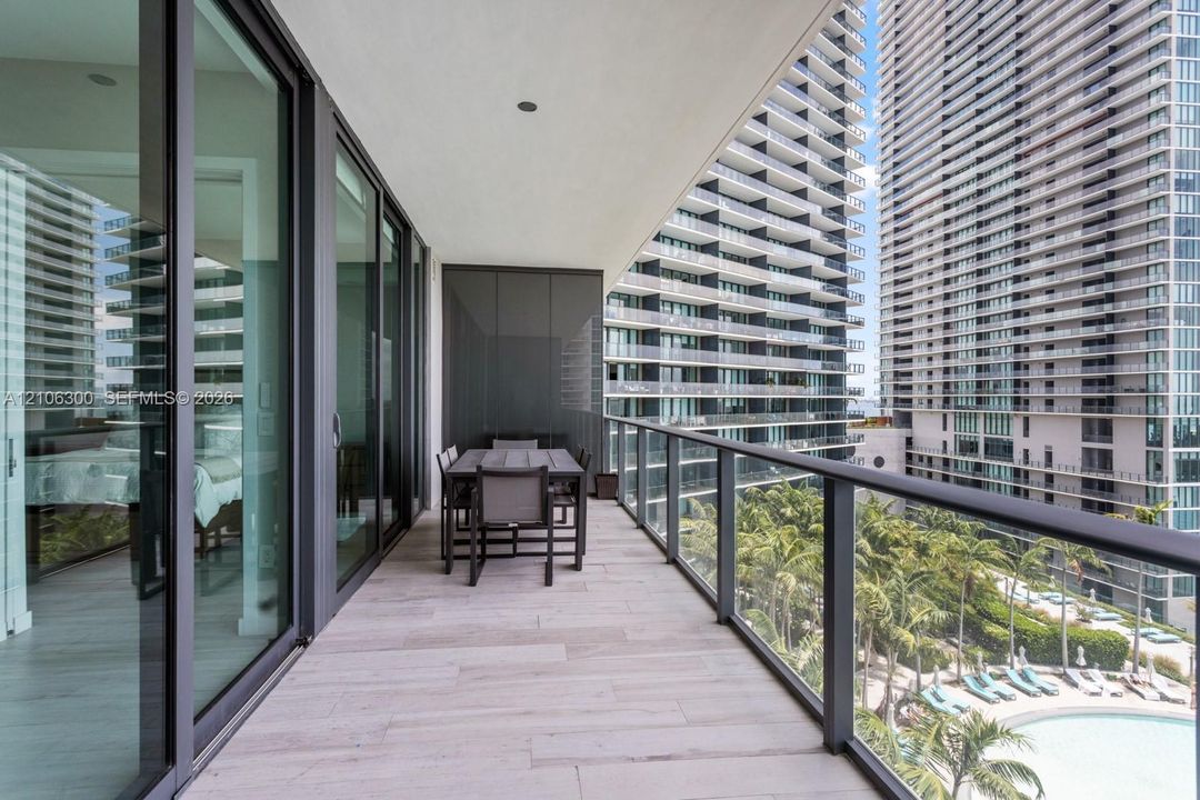 Covered balcony featuring wood-finish tile flooring, glass railings, and expansive sliding glass doors