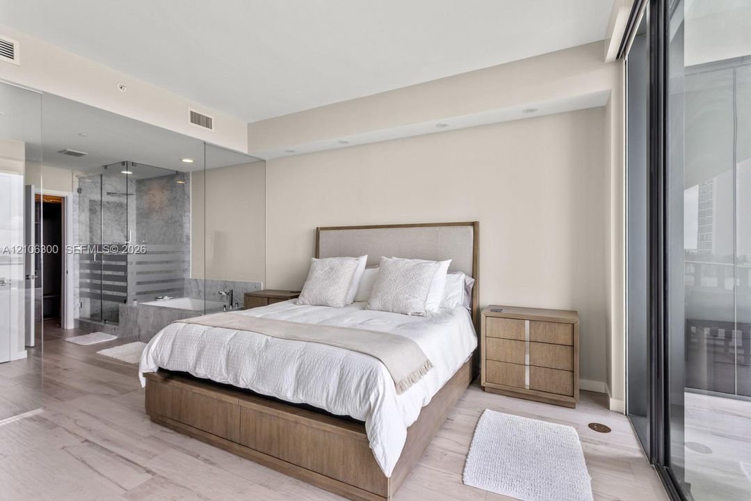 Neutral-toned interior featuring wood-finish flooring, full-height glass partitions, a glass-enclosed shower, and expansive sliding glass doors