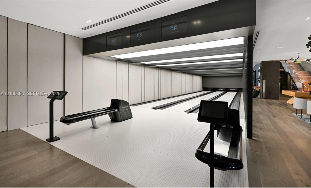 Private three-lane bowling alley featuring recessed linear lighting, integrated electronic scoring consoles, wood-finish flooring, and minimalist paneled walls