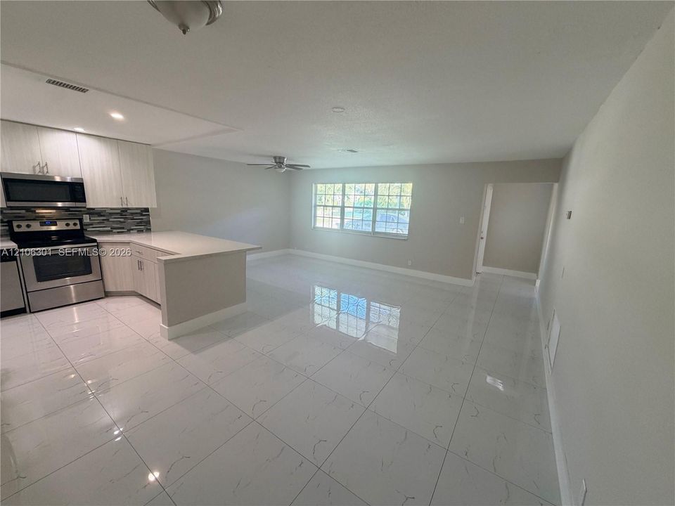 Kitchen featuring light-toned cabinetry, a stone-surface peninsula, stainless steel appliances, a multi-tonal tile backsplash, and large-format tile flooring