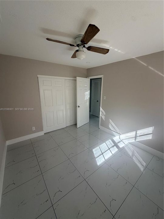 Room featuring polished stone-finish tile flooring, ceiling fan with integrated lighting, and multi-panel bi-fold closet doors