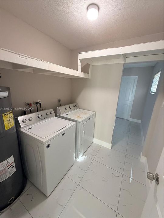Laundry area featuring large-format porcelain tile flooring, built-in overhead storage shelving, and ceiling-mounted dome lighting